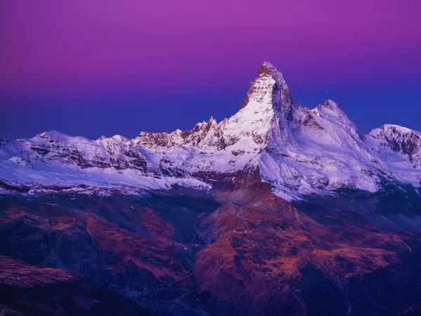Matterhorn mountain peak glowing under a vivid purple and pink twilight sky in the Swiss Alps near Zermatt