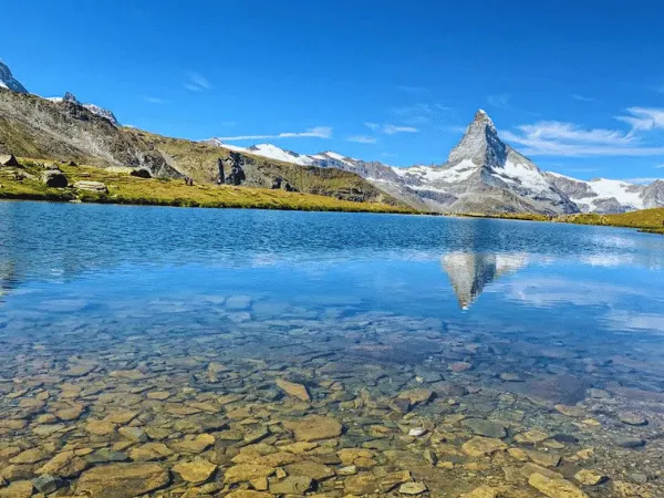 Crystal clear shallow alpine lake reflecting the Matterhorn peak under a bright blue sky on the Five Lakes Walk in Zermatt