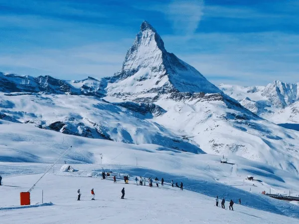 Skiers on wide snowy pistes at Zermatt ski resort with the Matterhorn peak rising sharply against a blue sky
