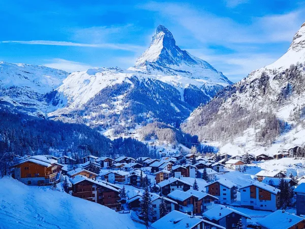 Snow-covered chalets of Zermatt village in winter daylight with the Matterhorn summit visible above the surrounding alpine slopes