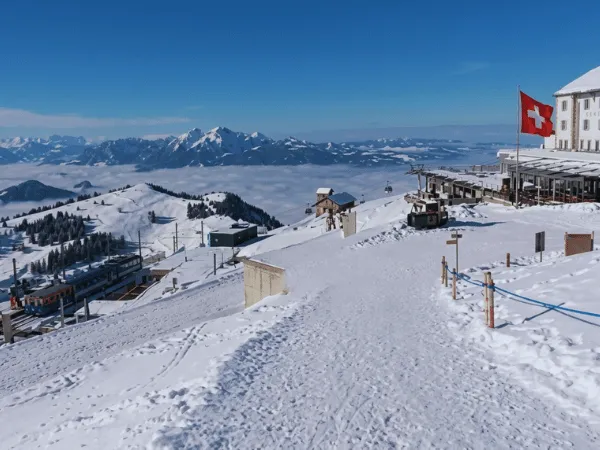 snow-covered-rigi-kulm-summit-above-clouds-with-swiss-flag-in-winter