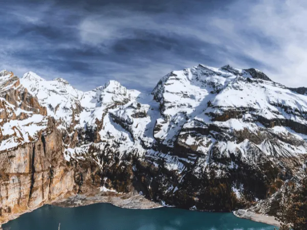 aerial drone view of oeschinensee kandersteg with snow-covered mountains and turquoise glacial lake under dramatic cloudy sky switzerland