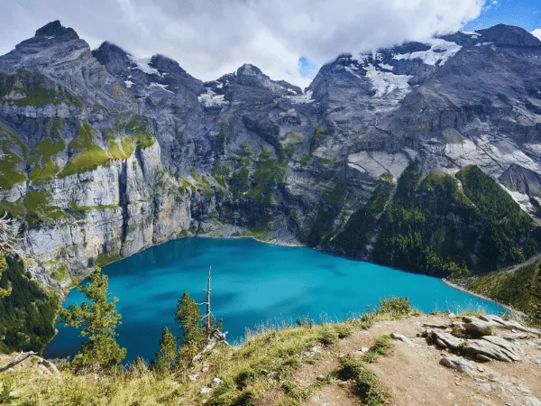 elevated hiking trail viewpoint above oeschinensee kandersteg showing vivid turquoise lake surrounded by dramatic limestone walls and glaciated peaks switzerland