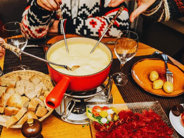 group-of-people-dipping-bread-into-a-red-pot-of-swiss-cheese-fondue-with-bread-basket-and-wine-glasses-on-the-table
