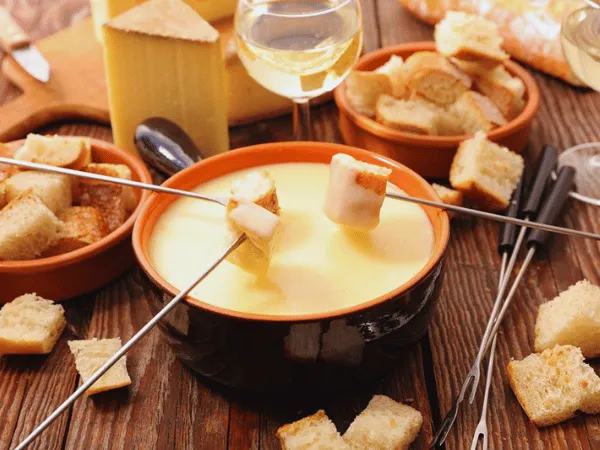 swiss-cheese-fondue-in-an-orange-pot-with-bread-cubes-fondue-forks-and-white-wine-on-a-wooden-table