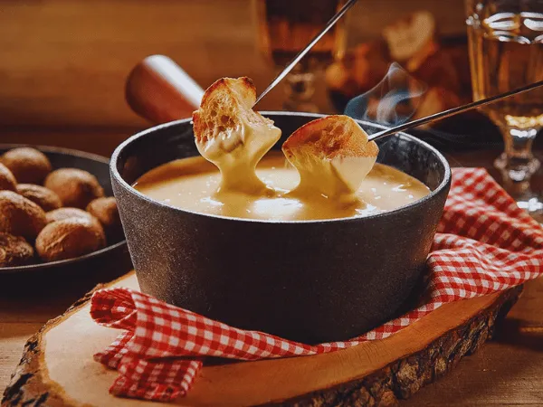 close-up-of-traditional-swiss-cheese-fondue-with-bread-pieces-on-fondue-forks-in-a-black-pot