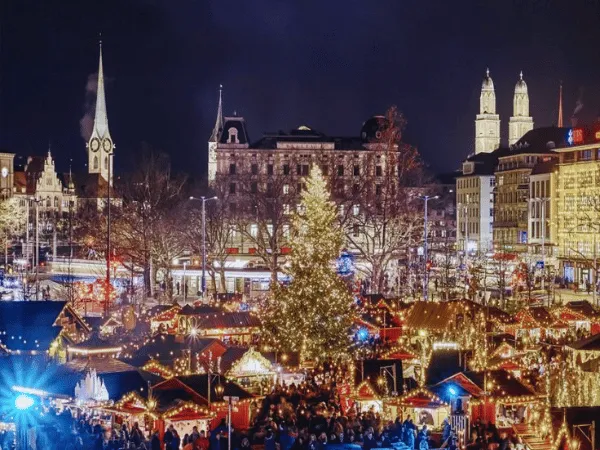 aerial-night-view-of-zurich-christmas-market-with-festive-lights-and-grossmunster-cathedral-towers