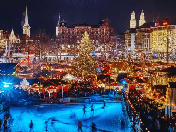 zurich-christmas-market-at-night-with-ice-skating-rink-festive-lights-and-grossmunster-cathedral
