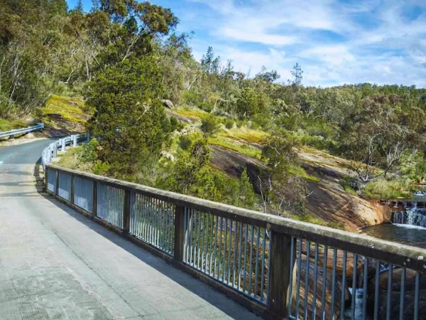 Road bridge with metal railings over Rocky Valley Creek with a small waterfall over granite rocks and native bushland in the background near the Beechworth Gorge Walk trailhead