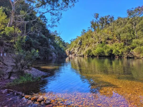 Clear blue waters of Spring Creek flowing through the rocky granite gorge on the Beechworth Gorge Walk in northeast Victoria under a bright blue sky
