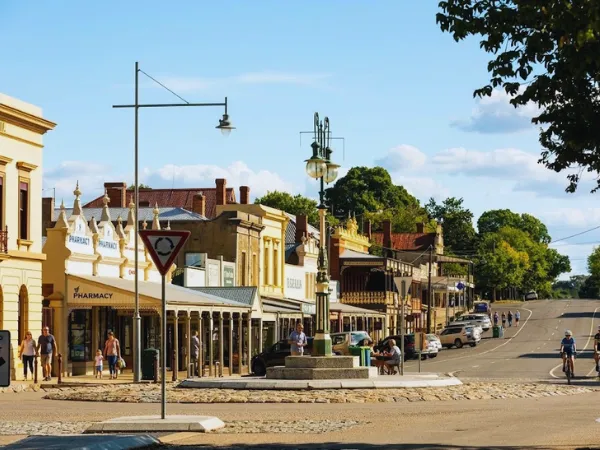 Sunlit heritage streetscape of Ford Street Beechworth Victoria with gold rush era yellow buildings cyclists and pedestrians on a clear summer day