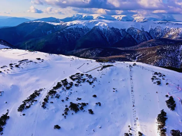 Aerial view of snow-covered slopes at Falls Creek with the Bogong High Plains in the background