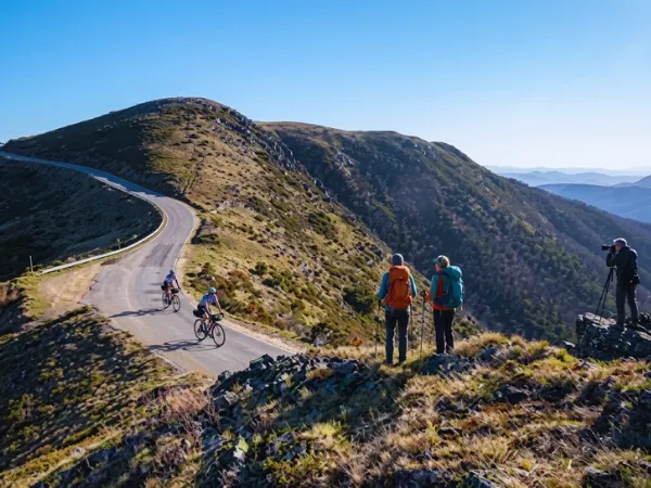 Hikers with backpacks and a photographer standing on a rocky ridge above the Great Alpine Road at Mt Hotham with panoramic mountain views