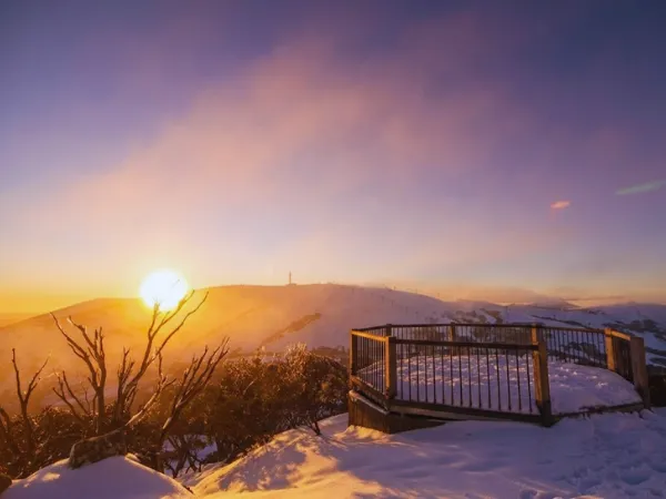 Golden winter sunrise over snow-covered Mt Hotham lookout platform with purple and orange sky reflecting across the snowfields