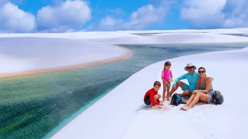 Family sitting on white sand dunes above a lagoon in Lençóis Maranhenses