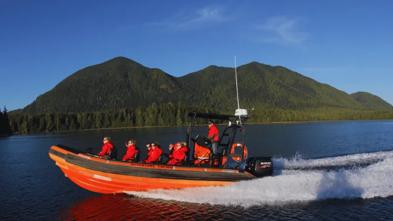 Orange zodiac boat with tourists cruising near forested coastline in Tofino Canada