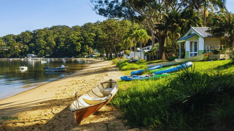 Dangar Island NSW beach with kayaks, boats, and a green cottage