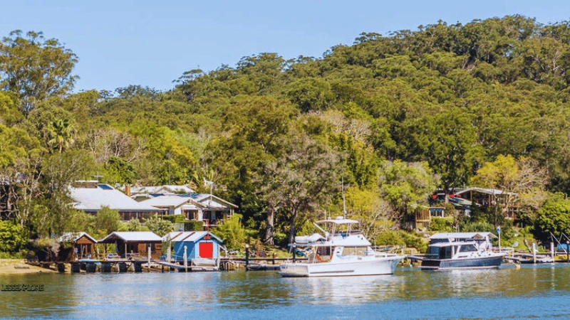 Boat sheds and boats moored along Dangar Island NSW riverbank