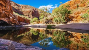 Ormiston Gorge waterhole reflecting red cliffs, ghost gums, and a blue sky with white clouds